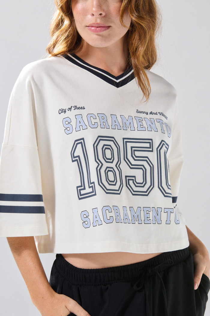 Camiseta oversize crop top crema con cuello V y arte college
