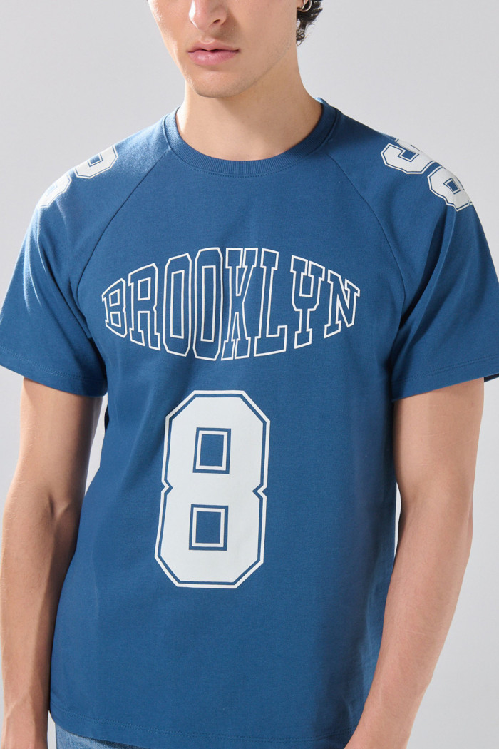 Camiseta azul con manga ranglan y diseños college
